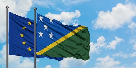 European Union and Solomon Islands flag waving in the wind against white cloudy blue sky together....