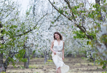 Fototapeta na wymiar A beautiful young Caucasian woman with curly dark hair walking in blossoming orchard