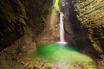 Mystical view of the rocky amphitheatre with a green pool and a white beam of water. 15-metre-high Kozjak Waterfall (Slap Kozjak). Famous touristic place and travel destination in Slovenia