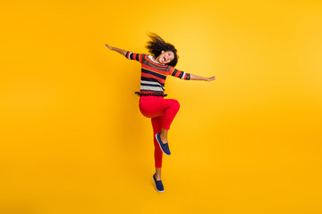 Fototapeta na wymiar Full size photo of cheerful crazy afro american girl have autumn holidays hold hands imagine she bird feel inspired scream wear red pants trousers modern fall outfit isolated yellow color background