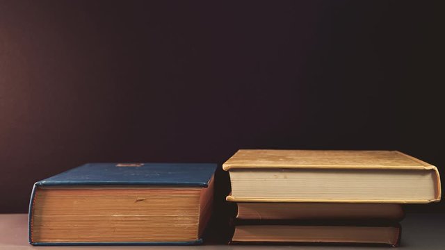 Stop motion stacking old books on a black background. growing book pile on a bookshelf.