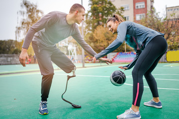 Young man with prosthetic leg enjoying with his friend at basketball court.