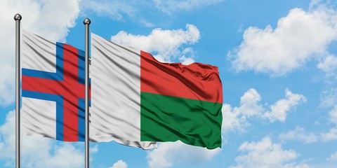 Faroe Islands and Madagascar flag waving in the wind against white cloudy blue sky together....