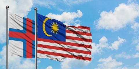 Faroe Islands and Malaysia flag waving in the wind against white cloudy blue sky together....