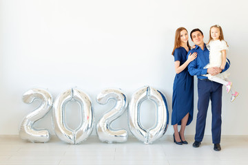 Young happy family mother and father and daughter standing near balloons shaped like numbers 2020...