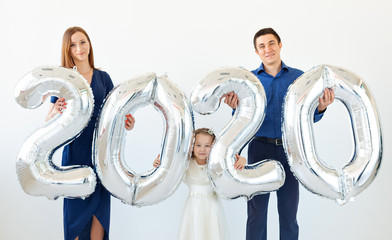Young happy family mother and father and daughter holding balloons shaped like numbers 2020 on...