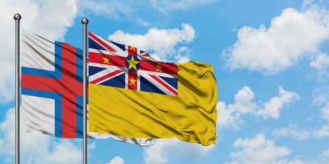 Faroe Islands and Niue flag waving in the wind against white cloudy blue sky together. Diplomacy...
