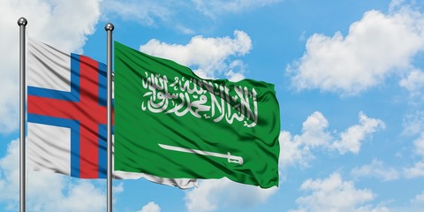 Faroe Islands and Saudi Arabia flag waving in the wind against white cloudy blue sky together. Diplomacy concept, international relations.