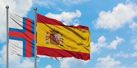 Faroe Islands and Spain flag waving in the wind against white cloudy blue sky together. Diplomacy concept, international relations.