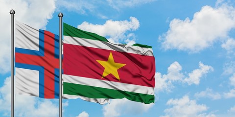 Faroe Islands and Suriname flag waving in the wind against white cloudy blue sky together. Diplomacy concept, international relations.