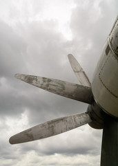 Part of the fuselage of the old military plane with the propeller closeup against the background of an empty and gray sky.