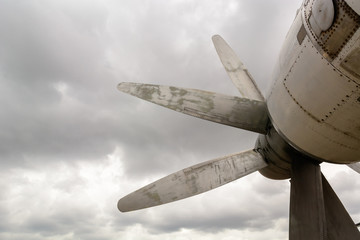 Part of the fuselage of the old military plane with the propeller closeup against the background of an empty and gray sky.
