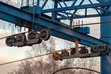 A roller system with cables for Ski lift close-up. Blue bars with mounts. Blurry trees on the background.