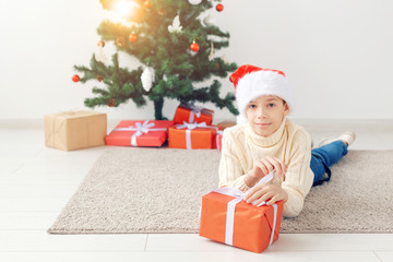 Obraz na płótnie Canvas Holidays, christmas, childhood and people concept - smiling happy teen boy in santa hat with gift box over christmas tree background