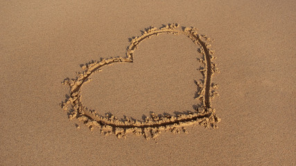Perfectly drawn heart shape in the golden sand on the beach, concept for romantic love, friendship, wedding, or marriage and honeymoon in the sun, neat background with hand sand writing and copy space