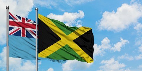 Fiji and Jamaica flag waving in the wind against white cloudy blue sky together. Diplomacy concept, international relations.