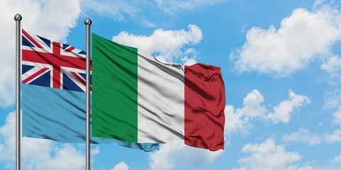 Fiji and Italy flag waving in the wind against white cloudy blue sky together. Diplomacy concept, international relations.