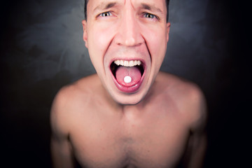 a man without clothes shows his tongue on which lies a pill