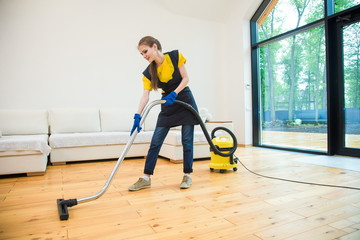 professional cleaning service. woman in uniform and gloves does the cleaning in a cottage. the worker vacuums the floor with professional equipment