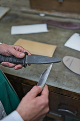 Craftsman's hands sharpening the edge of the cutter with a knife whetstone to better cut the tool. Vertical photo