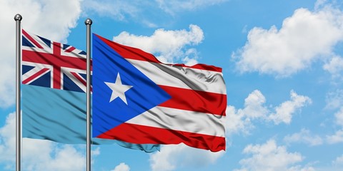 Fiji and Puerto Rico flag waving in the wind against white cloudy blue sky together. Diplomacy concept, international relations.