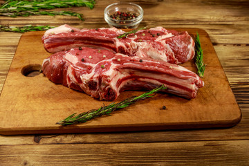 Raw fresh beef rib eye steaks on bone with spices and rosemary on wooden table