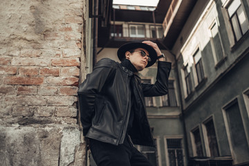 Fototapeta na wymiar Portrait of Stylish Young Man in Black Leather Jacket and Hat
