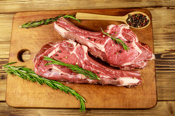 Raw fresh beef rib eye steaks on bone with spices and rosemary on wooden table. Top view