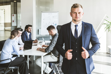 Business man stands on the background of partners. A team of young businessmen working and communicating together in an office. Corporate businessteam and manager in a meeting.