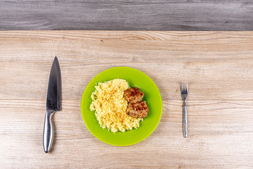 Millet porridge with minced pork cutlets on a plate on the table with a fork and a knife