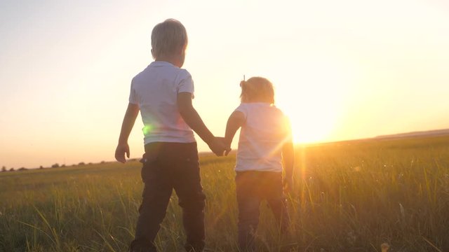 happy family teamwork brother and sister hold hands walk in the park at sunset on the grass. slow motion video little girl and boy walking in nature lifestyle outdoors