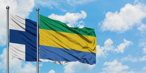 Finland and Gabon flag waving in the wind against white cloudy blue sky together. Diplomacy...