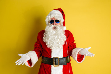 Santa Claus with modern eyeglasses isolated on yellow studio background. Caucasian male model in traditional costume. Concept of Christmas, New Year's, winter mood, technologies. Astonished and