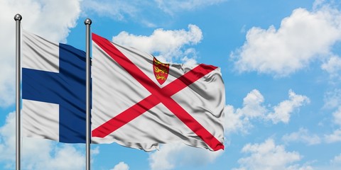 Finland and Jersey flag waving in the wind against white cloudy blue sky together. Diplomacy...