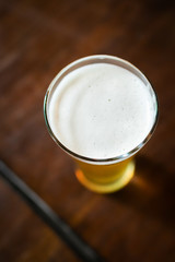 Glass of beer with foam on wooden table. Overhead shot.