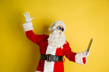 Fototapeta na wymiar Santa Claus with modern gadgets isolated on yellow studio background. Caucasian male model in traditional costume. Concept of Christmas, New Year's, winter mood, technologies. Making selfie or vlog.