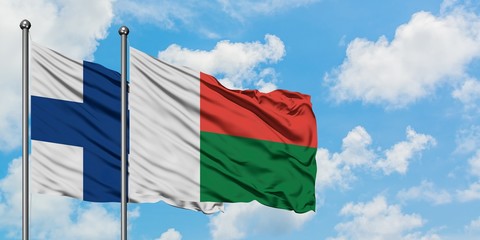 Finland and Madagascar flag waving in the wind against white cloudy blue sky together. Diplomacy...