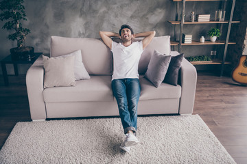 Obraz premium Photo of mixed race arabian guy sitting cozy sofa holding hands behind head relaxing homey weekend mood looking dreamy up wear casual outfit flat loft living room indoors