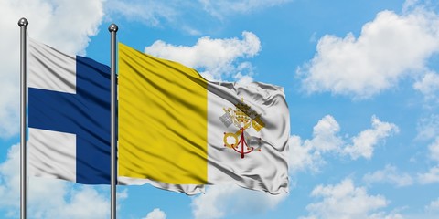 Finland and Vatican City flag waving in the wind against white cloudy blue sky together. Diplomacy...