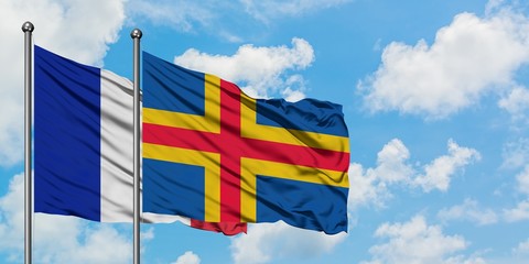 France and Aland Islands flag waving in the wind against white cloudy blue sky together. Diplomacy...
