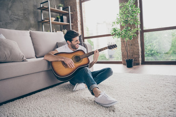 Photo of mixed race guy sitting floor leaning sofa hold acoustic instrumental guitar playing new written song sound signing creative talented person flat loft living room indoors