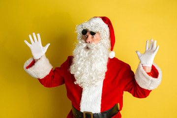 Santa Claus with modern eyeglasses isolated on yellow studio background. Caucasian male model in traditional costume. Concept of Christmas, New Year's, winter mood, technologies. Astonished and