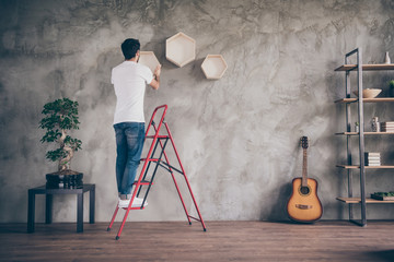 Full length rear behind view photo of mixed race arabian guy installing wall shelf standing on...