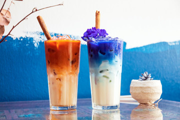 Iced milk tea and butterfly pea latte with cinnamon stick on table and paint blue color wall...