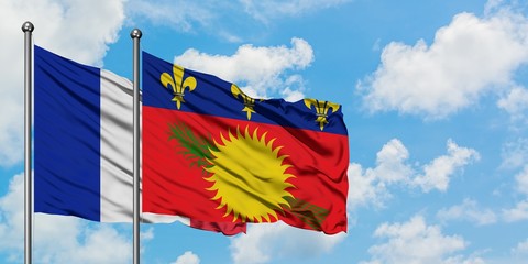 France and Guadeloupe flag waving in the wind against white cloudy blue sky together. Diplomacy concept, international relations.