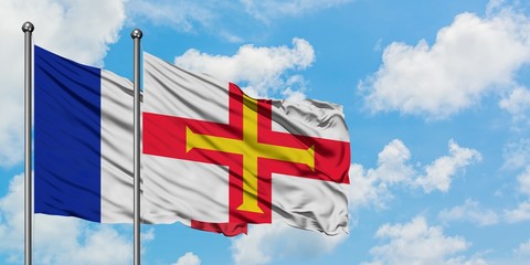 France and Guernsey flag waving in the wind against white cloudy blue sky together. Diplomacy...
