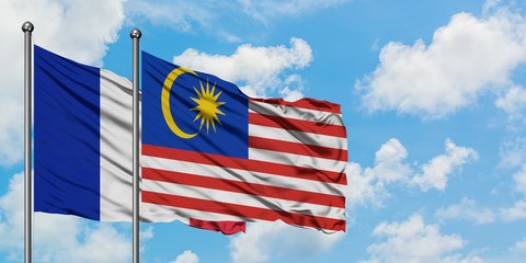France and Malaysia flag waving in the wind against white cloudy blue sky together. Diplomacy concept, international relations.