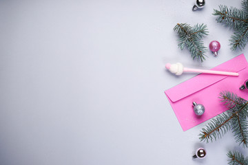 Christmas composition. A branch of blue pine, pink envelope, pink pen, Christmas balls on a gray background. Place for text, flat lay.