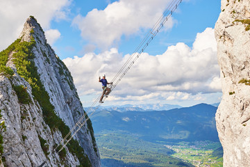 Intersport Donnerkogel via ferrata in Summer, with a man showing a victory sign while climbing the diagonal ladder. Stairway to heaven concept.