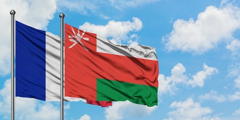 France and Oman flag waving in the wind against white cloudy blue sky together. Diplomacy concept, international relations.